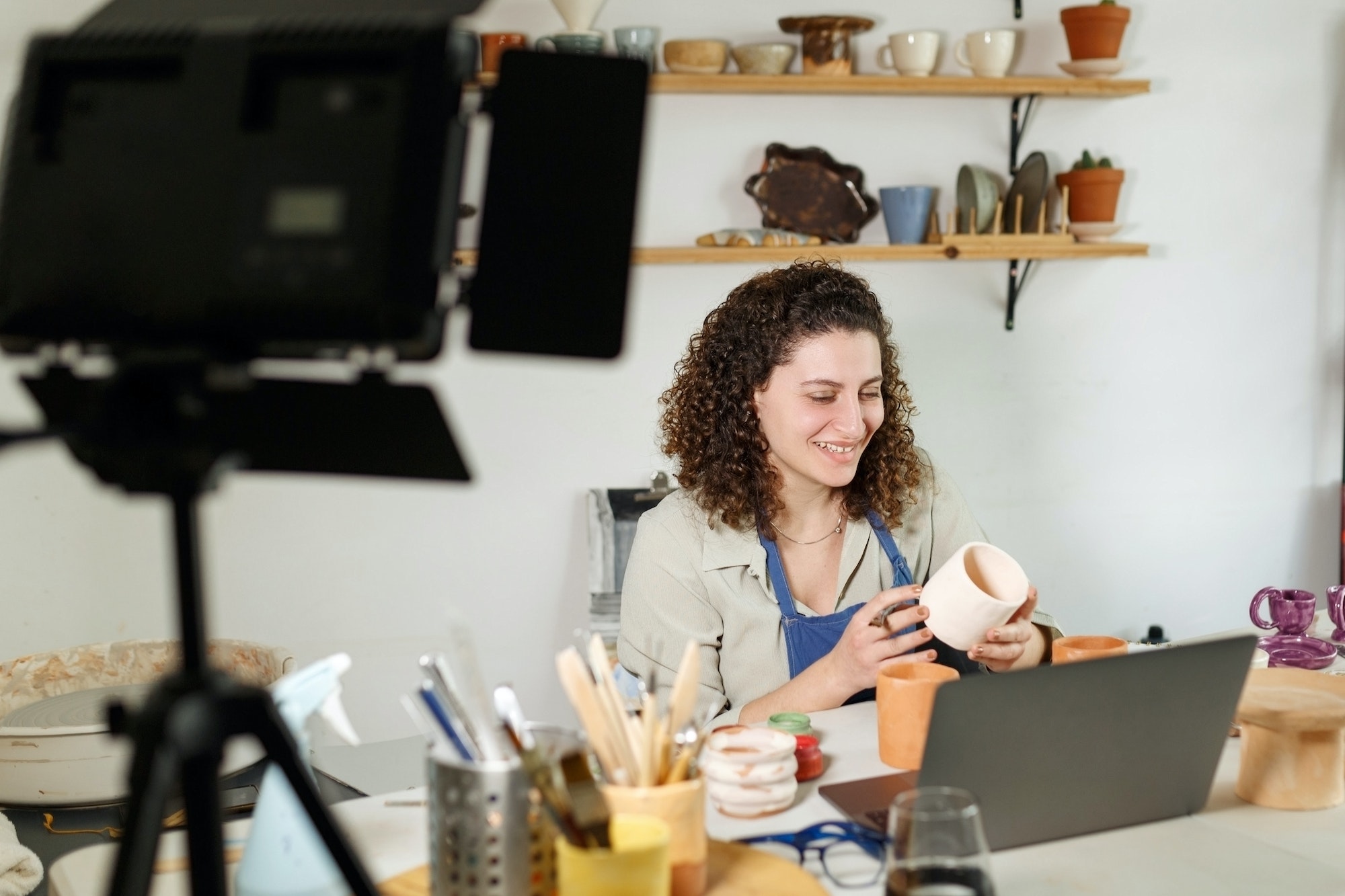 Females potter in blue apron making a vlog, recording online course, clay master class.